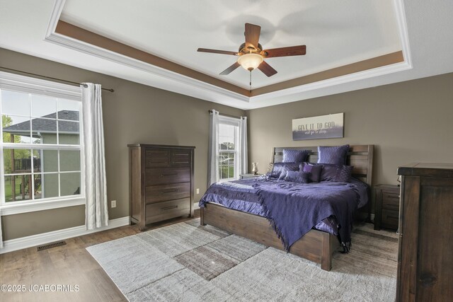 bedroom featuring a tray ceiling, a ceiling fan, visible vents, baseboards, and wood finished floors