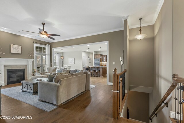 living room featuring ceiling fan, a high end fireplace, baseboards, dark wood-style flooring, and ornamental molding