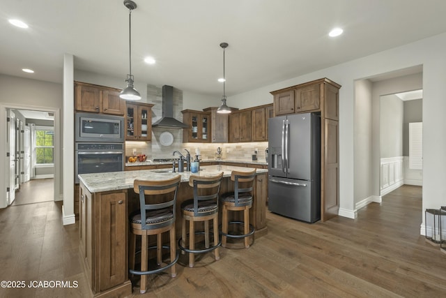 kitchen with dark wood-style flooring, stainless steel appliances, glass insert cabinets, tasteful backsplash, and wall chimney range hood