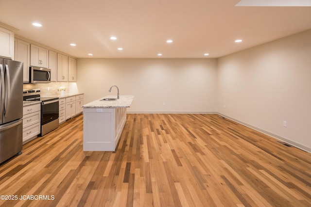 kitchen with stainless steel appliances, white cabinetry, a sink, an island with sink, and light stone countertops