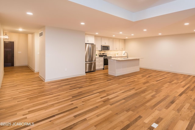 kitchen featuring white cabinetry, open floor plan, appliances with stainless steel finishes, light stone countertops, and an island with sink