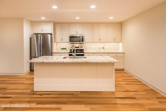 kitchen with a center island with sink, appliances with stainless steel finishes, light stone counters, white cabinetry, and backsplash