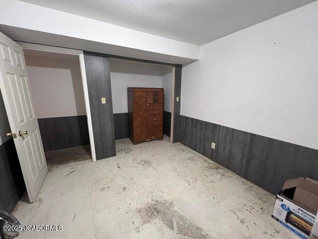 unfurnished bedroom featuring a wainscoted wall and unfinished concrete floors