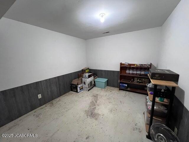 unfurnished room featuring concrete flooring and a wainscoted wall