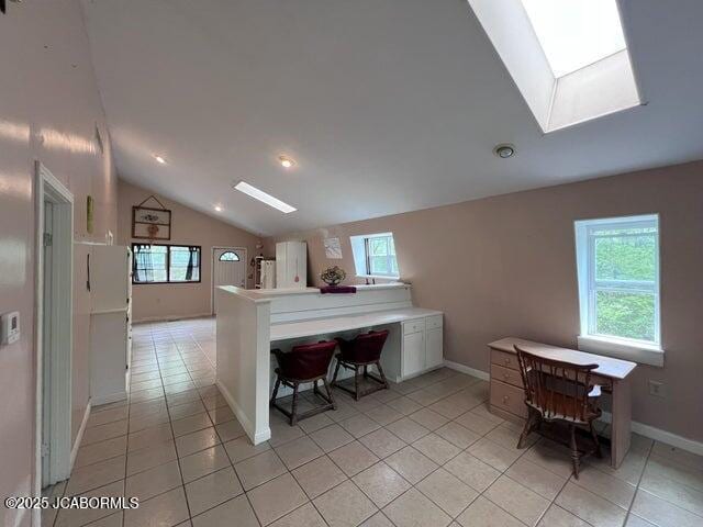 kitchen featuring a skylight, vaulted ceiling, light tile patterned floors, white cabinets, and baseboards