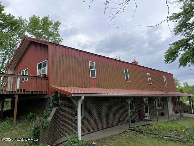 view of front of house featuring a patio area, a deck, metal roof, and a chimney
