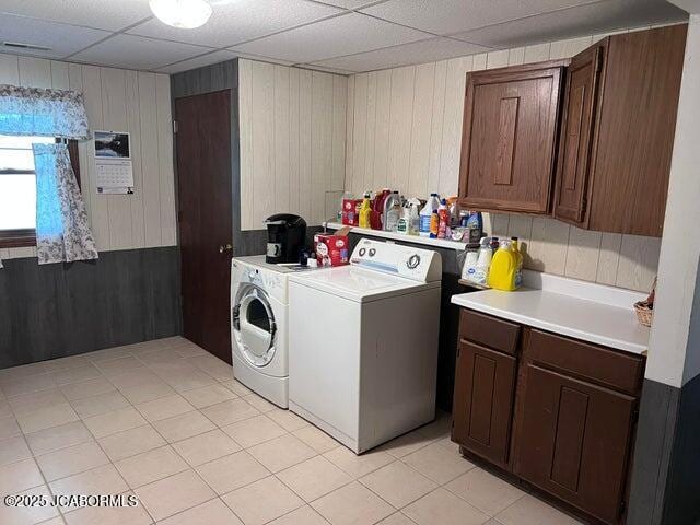 clothes washing area featuring separate washer and dryer, cabinet space, wooden walls, and light tile patterned floors