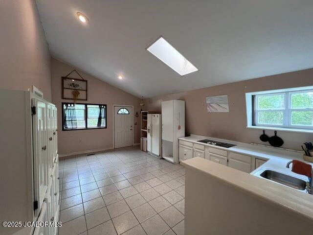 kitchen featuring white refrigerator with ice dispenser, a skylight, a sink, vaulted ceiling, and light tile patterned floors