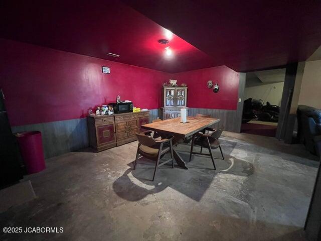 dining space featuring concrete floors and a wainscoted wall
