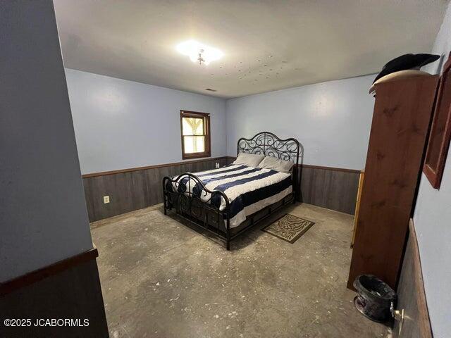 bedroom featuring wainscoting, wood walls, and concrete flooring