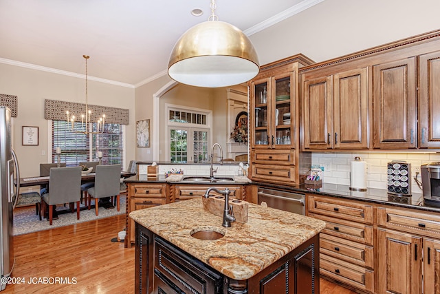 kitchen featuring backsplash, sink, dark stone countertops, an island with sink, and decorative light fixtures