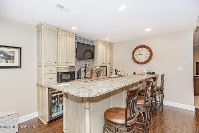 kitchen with a kitchen breakfast bar, sink, hanging light fixtures, light stone counters, and dark hardwood / wood-style flooring