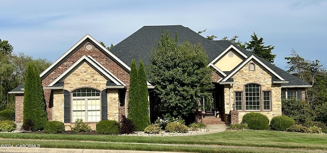 exterior space with a shingled roof, stone siding, brick siding, and a front lawn