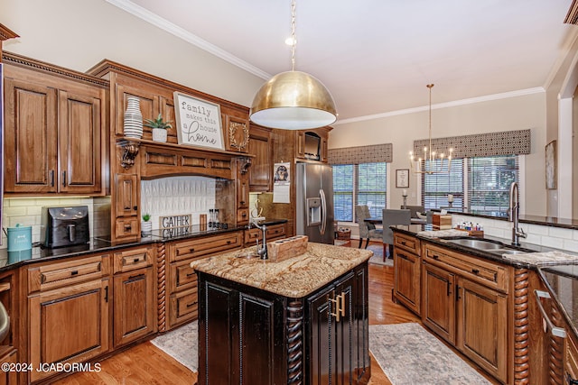 kitchen with dark stone counters, sink, a center island with sink, decorative light fixtures, and stainless steel fridge with ice dispenser