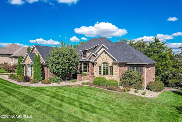 view of front of home featuring a shingled roof, stone siding, brick siding, and a front lawn