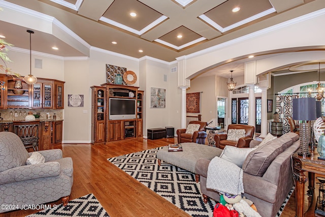 living room with coffered ceiling, a high ceiling, a notable chandelier, decorative columns, and ornamental molding