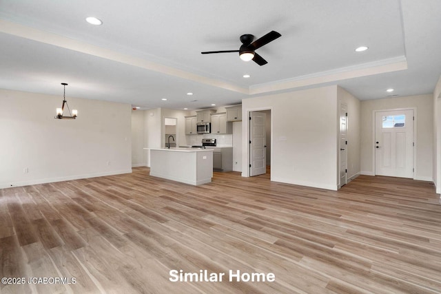 unfurnished living room with light wood finished floors, recessed lighting, ceiling fan with notable chandelier, and a raised ceiling