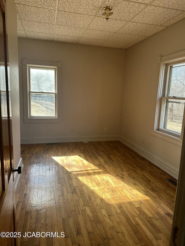 unfurnished room featuring a paneled ceiling, wood-type flooring, and plenty of natural light