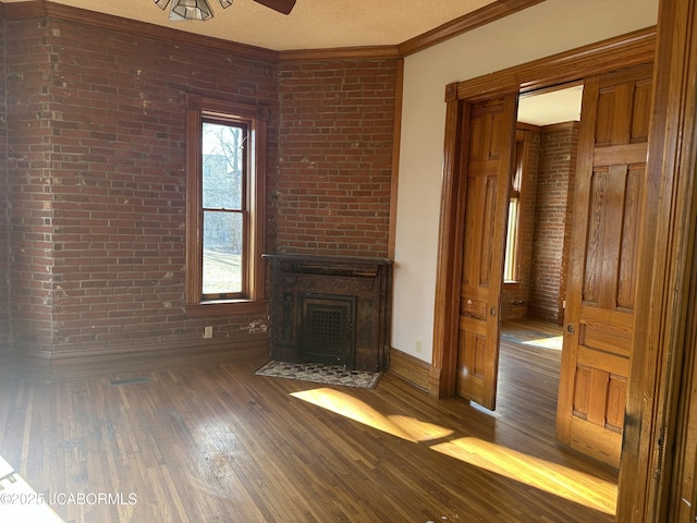 unfurnished living room featuring crown molding, brick wall, a large fireplace, and dark hardwood / wood-style flooring