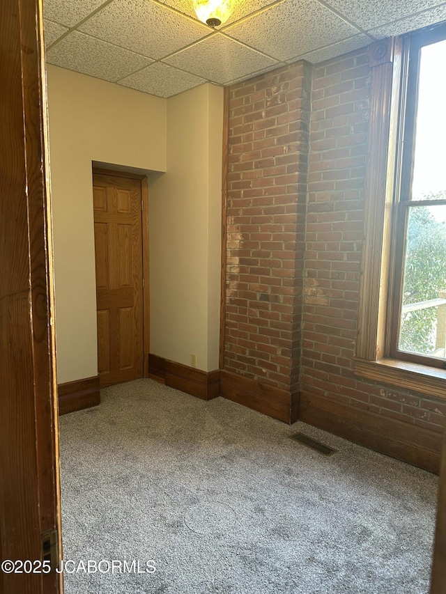 spare room featuring a paneled ceiling, brick wall, and carpet flooring