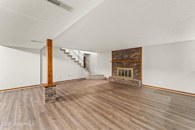 4300 W E Ridge Rd, Columbia, MO 65202 - unfurnished living room featuring wood finished floors, stairs, baseboards, a brick fireplace, and a textured ceiling