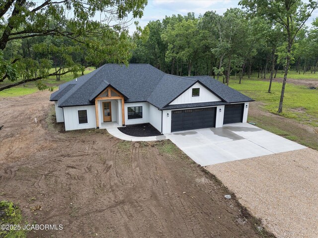 7058 County Road 409, Fulton, MO 65251 - modern farmhouse featuring concrete driveway, an attached garage, a shingled roof, a front yard, and view of wooded area