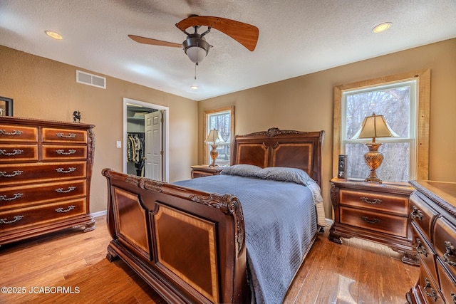 bedroom with a walk in closet, multiple windows, visible vents, and a textured ceiling