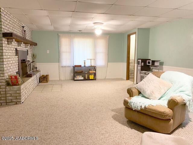 living area featuring light carpet, a paneled ceiling, and a wood stove