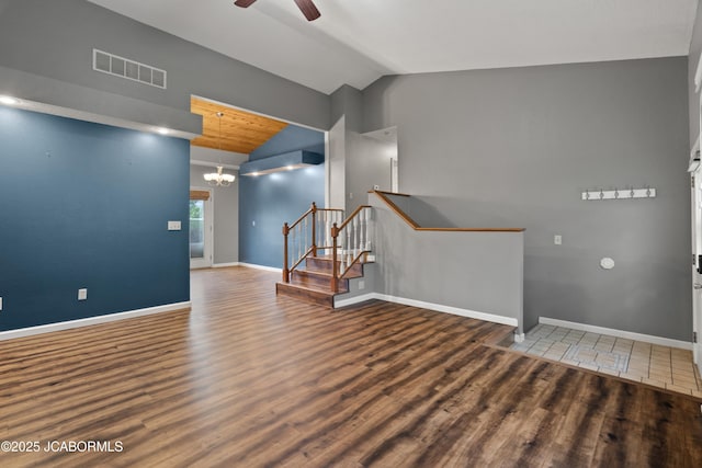 spare room with visible vents, vaulted ceiling, wood finished floors, stairway, and ceiling fan with notable chandelier