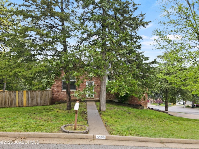 view of front of house featuring brick siding, fence, and a front yard