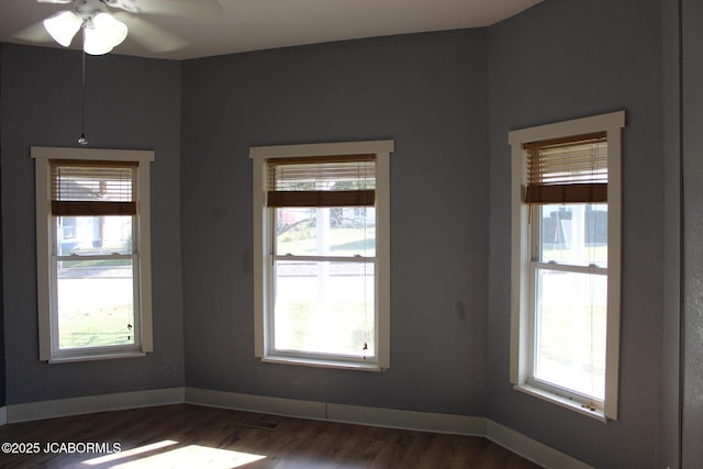 unfurnished room with a ceiling fan, dark wood-style flooring, a wealth of natural light, and baseboards