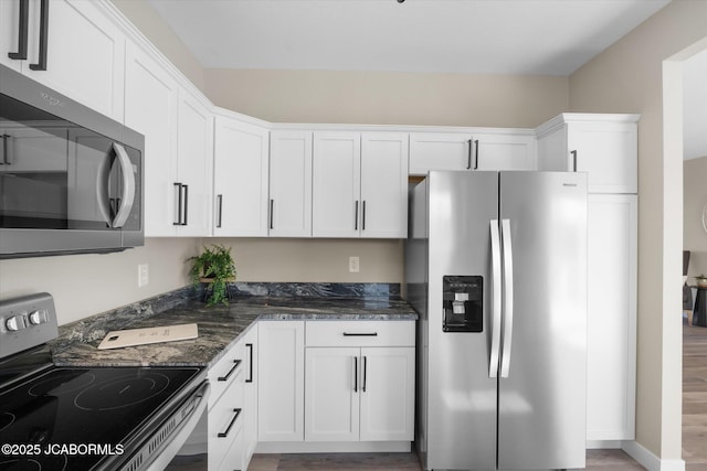 kitchen with stainless steel appliances, dark stone counters, and white cabinets