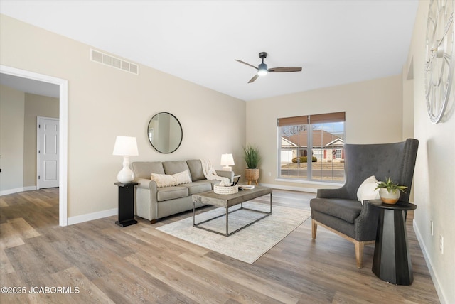 living area featuring a ceiling fan, visible vents, baseboards, and wood finished floors