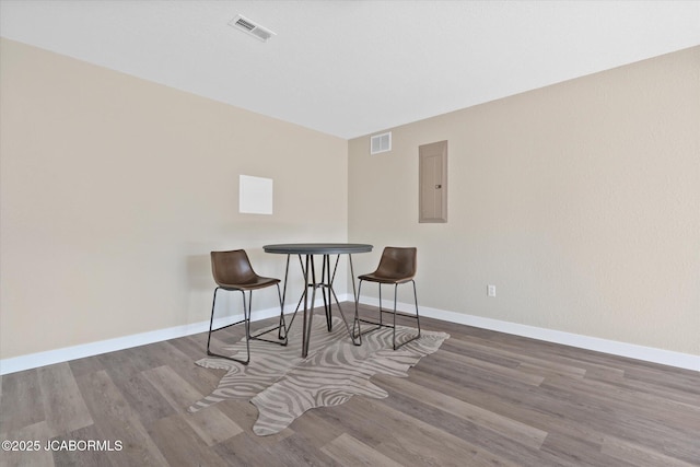 dining room featuring baseboards, wood finished floors, visible vents, and electric panel