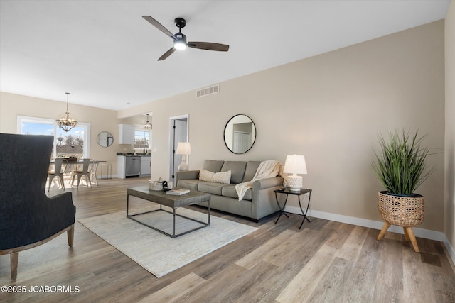 living room featuring light wood-style floors, baseboards, visible vents, and ceiling fan with notable chandelier