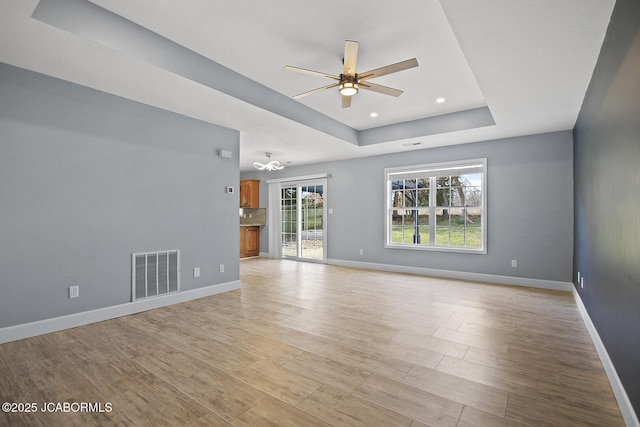 unfurnished room with light hardwood / wood-style floors, a raised ceiling, and ceiling fan