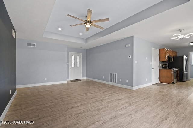 unfurnished living room with a tray ceiling, light hardwood / wood-style floors, and ceiling fan with notable chandelier