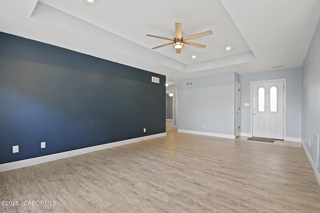 unfurnished living room featuring ceiling fan, light wood-type flooring, and a tray ceiling