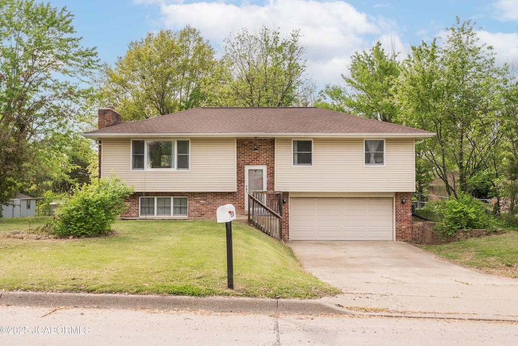 split foyer home with driveway, a chimney, a front yard, brick siding, and an attached garage