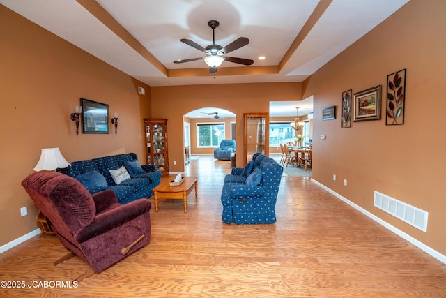 living area with a tray ceiling, visible vents, baseboards, and light wood-style floors