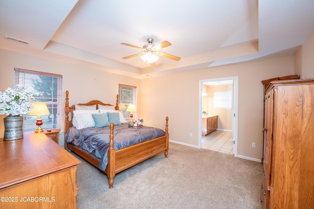 bedroom featuring visible vents, light colored carpet, a tray ceiling, and multiple windows