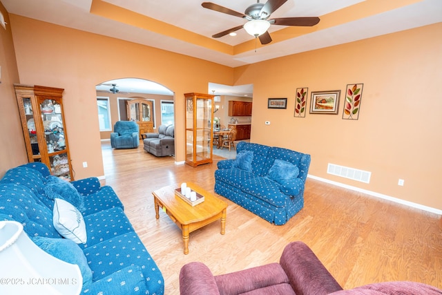 living room featuring arched walkways, visible vents, a raised ceiling, and wood finished floors