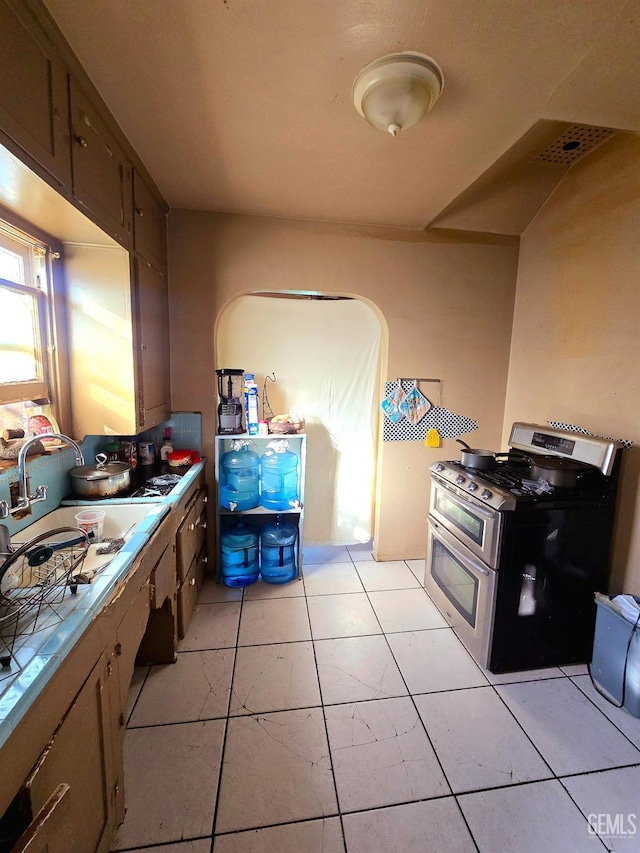 kitchen with tile countertops, light tile patterned floors, range with two ovens, a sink, and dark brown cabinetry