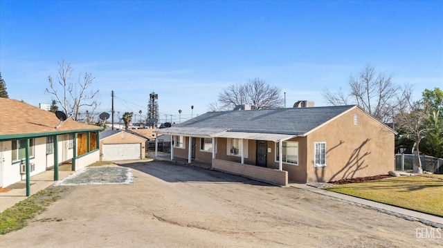 view of front facade featuring an outbuilding, covered porch, a detached garage, stucco siding, and a front yard