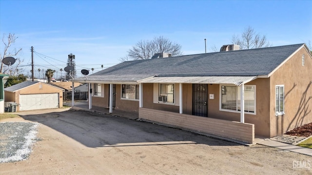 view of front facade featuring a porch, an outdoor structure, a detached garage, roof with shingles, and stucco siding