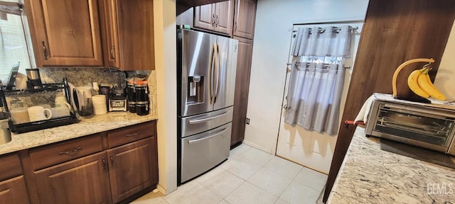 kitchen featuring decorative backsplash, stainless steel fridge, light tile patterned floors, and light stone counters