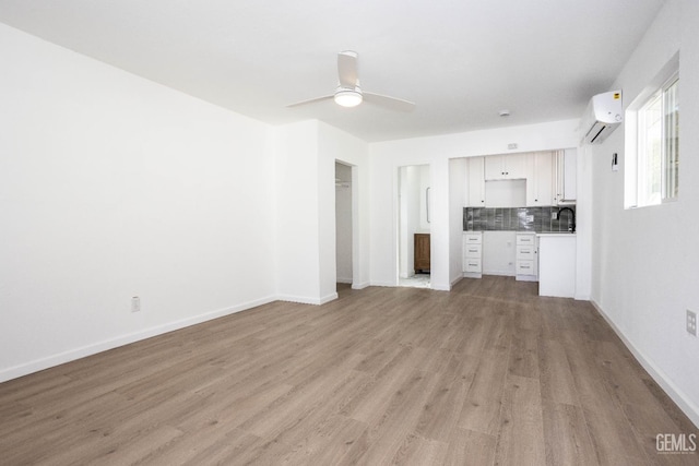 unfurnished living room featuring sink, light hardwood / wood-style flooring, a wall unit AC, and ceiling fan