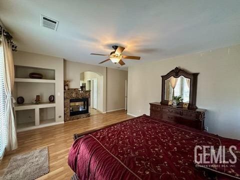 bedroom featuring arched walkways, a fireplace, visible vents, a ceiling fan, and wood finished floors