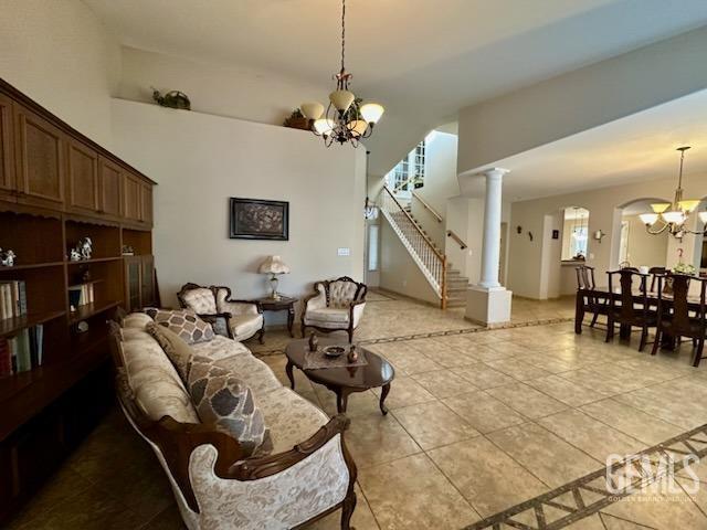 living area with light tile patterned floors, a notable chandelier, a towering ceiling, stairs, and decorative columns