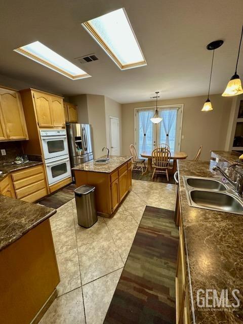 kitchen with a skylight, white double oven, visible vents, a sink, and stainless steel fridge